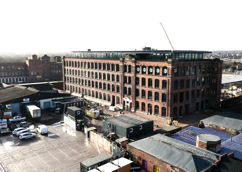 Wide exterior view of the multi-storey red brick Cotton Works building under a clear sky.