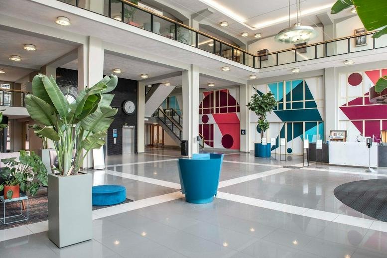 Spacious, modern lobby at Stationsplein 45 with high ceilings, colorful geometric murals, and potted plants.