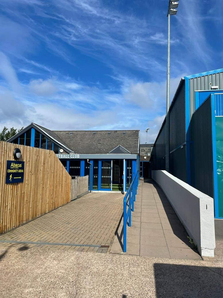 Entrance to the ARMCO Arena football club with blue framed windows and a wooden fence.