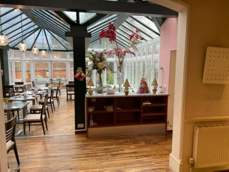 Spacious sunroom lounge at The Galaxie Hotel with a glass roof, wooden floors, and dining tables.