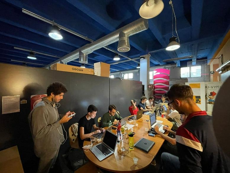 Vibrant communal coworking area with people working at a long wooden table under a blue ceiling.