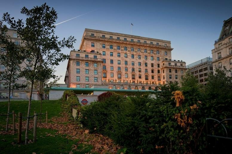 Grand stone exterior of Devonshire House viewed from a park at dusk.
