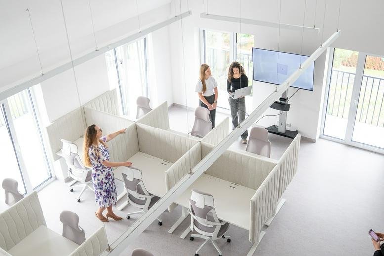 Spacious, high-ceiling coworking area at Dykova 1090/19 with modern cubicles and a wall-mounted presentation screen.