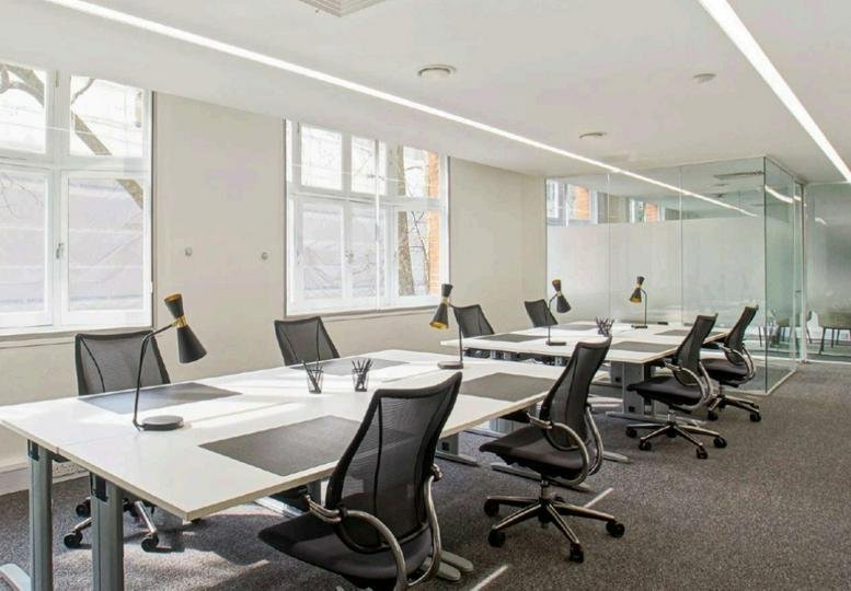 Bright open-plan office with white desks, ergonomic black chairs, and large windows.