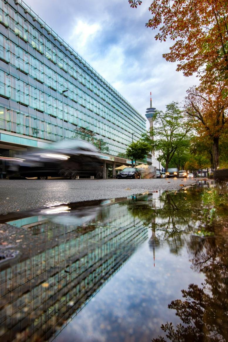 Exterior view of the modern glass-fronted office building at Hammer Straße 19 reflected in a rain puddle.