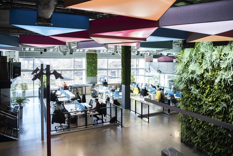 Spacious communal coworking area at Here East, Queen Elizabeth Olympic Park with colorful ceiling panels and green wall.
