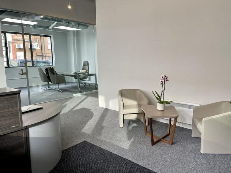 Reception lounge area with comfortable armchairs, a side table with flowers, and a view into a private office.