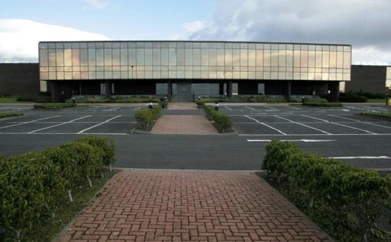 Exterior view of the glass-facade Mosshill Industrial Estate, Ayr, Scotland with a brick walkway and parking area.