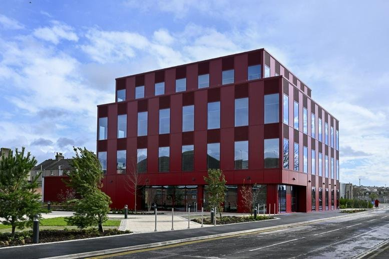 Exterior view of the modern red-cladded Innovation Centre, Central Way with large glass windows and blue sky.