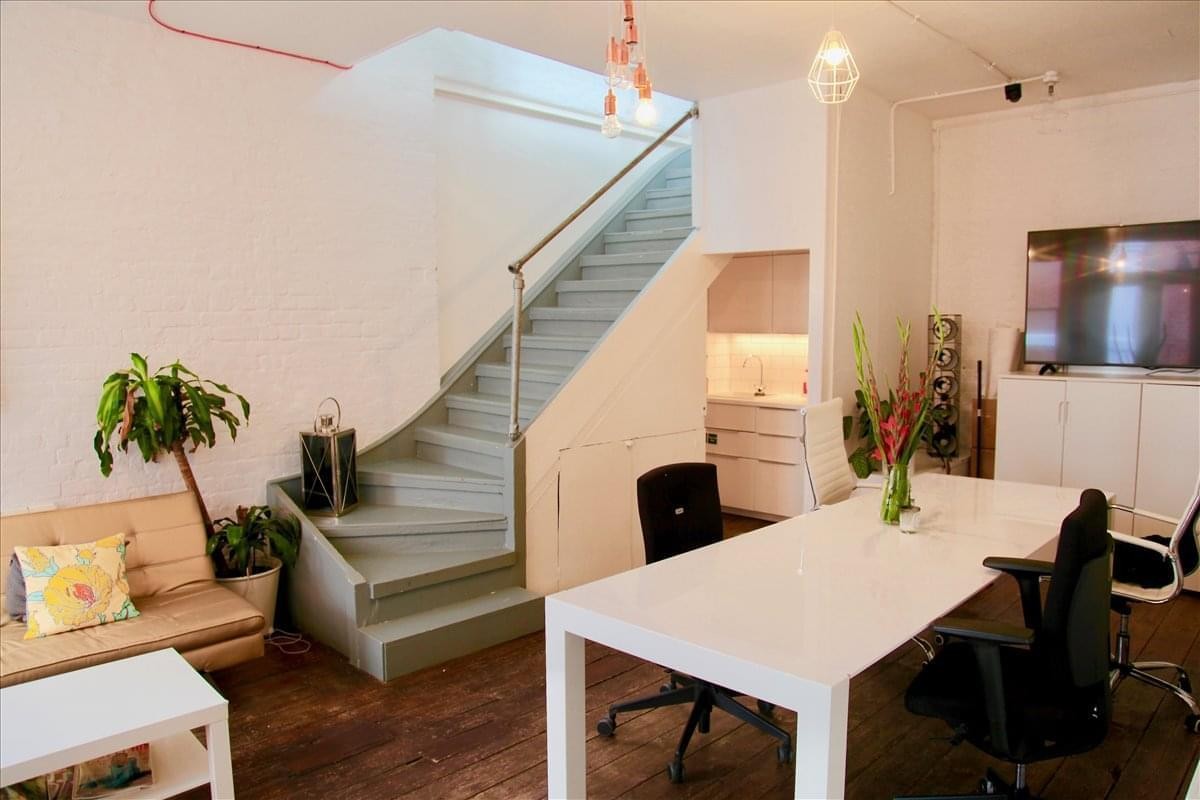 Modern office interior featuring a light blue staircase, a white communal table, and a lounge area with a sofa.
