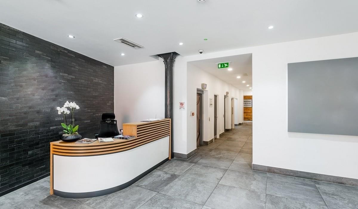 Reception area at 117-119 Portland Street featuring a curved white desk and a dark stone feature wall.