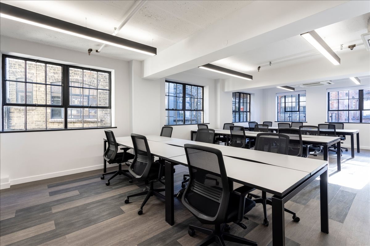 Spacious open-plan workspace at 21-22 Great Sutton Street with long white desks and large industrial windows.