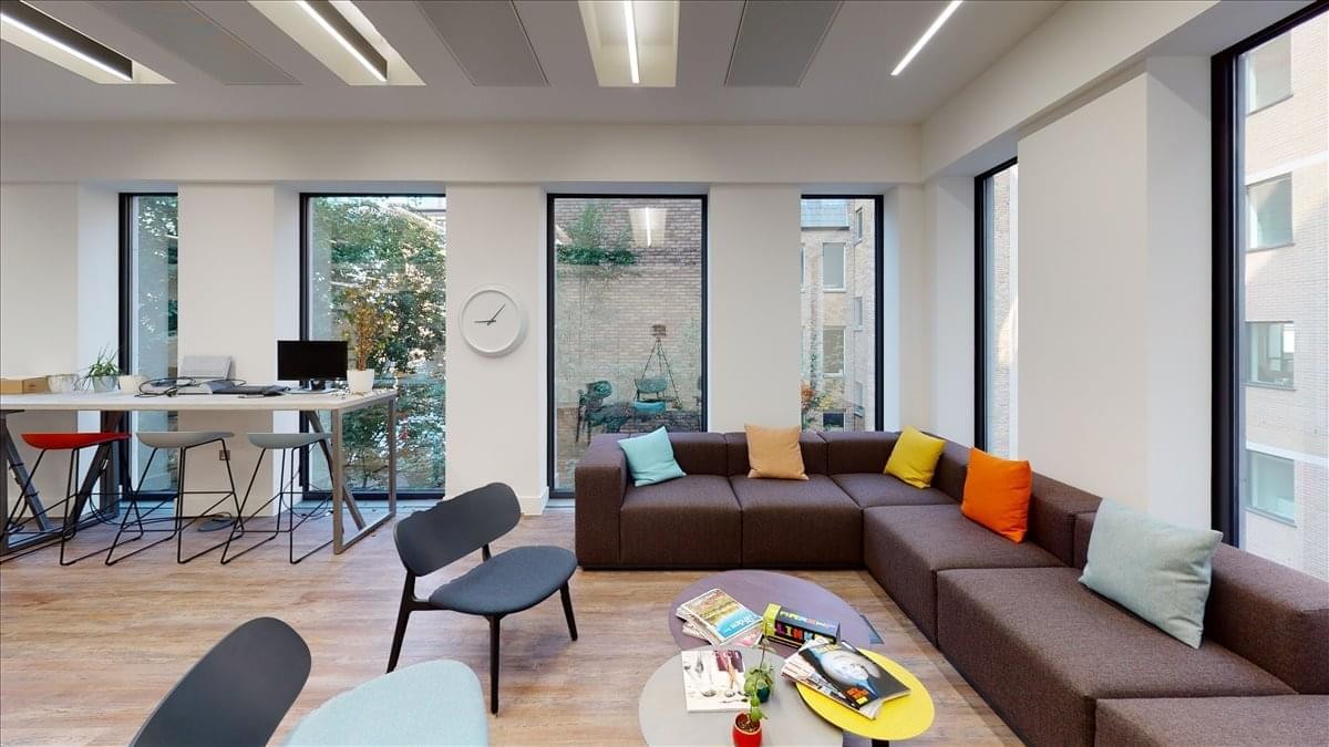 Bright breakout lounge with a large brown sectional sofa, colorful cushions, and floor-to-ceiling windows.