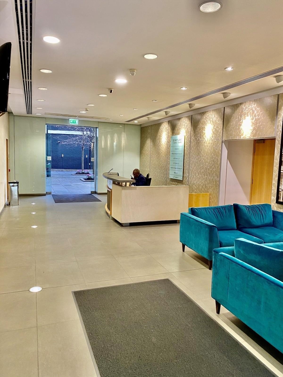 Bright reception area with a light wood desk, teal velvet sofas, and decorative patterned wallpaper.