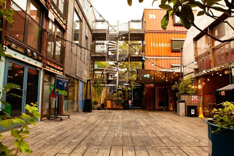 The courtyard entrance of Pop Brixton at 49 Brixton Station Road with shipping container offices and wooden decking.