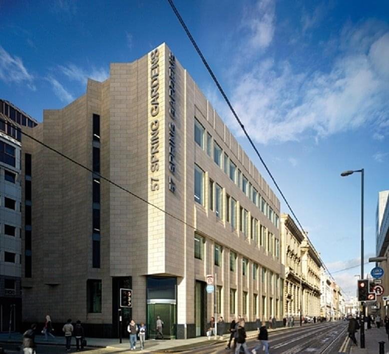 The sand-colored stone facade and entrance of the 57 Spring Gardens building against a blue sky.