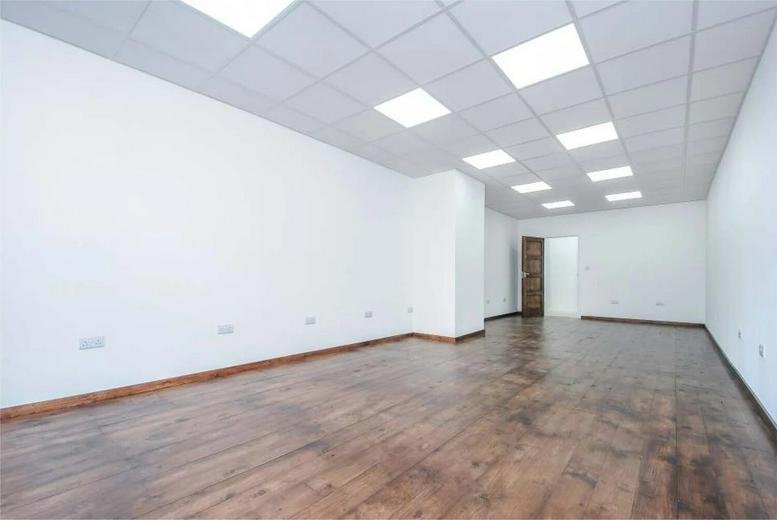 Spacious open-plan office featuring wood-effect flooring and bright LED ceiling panels.