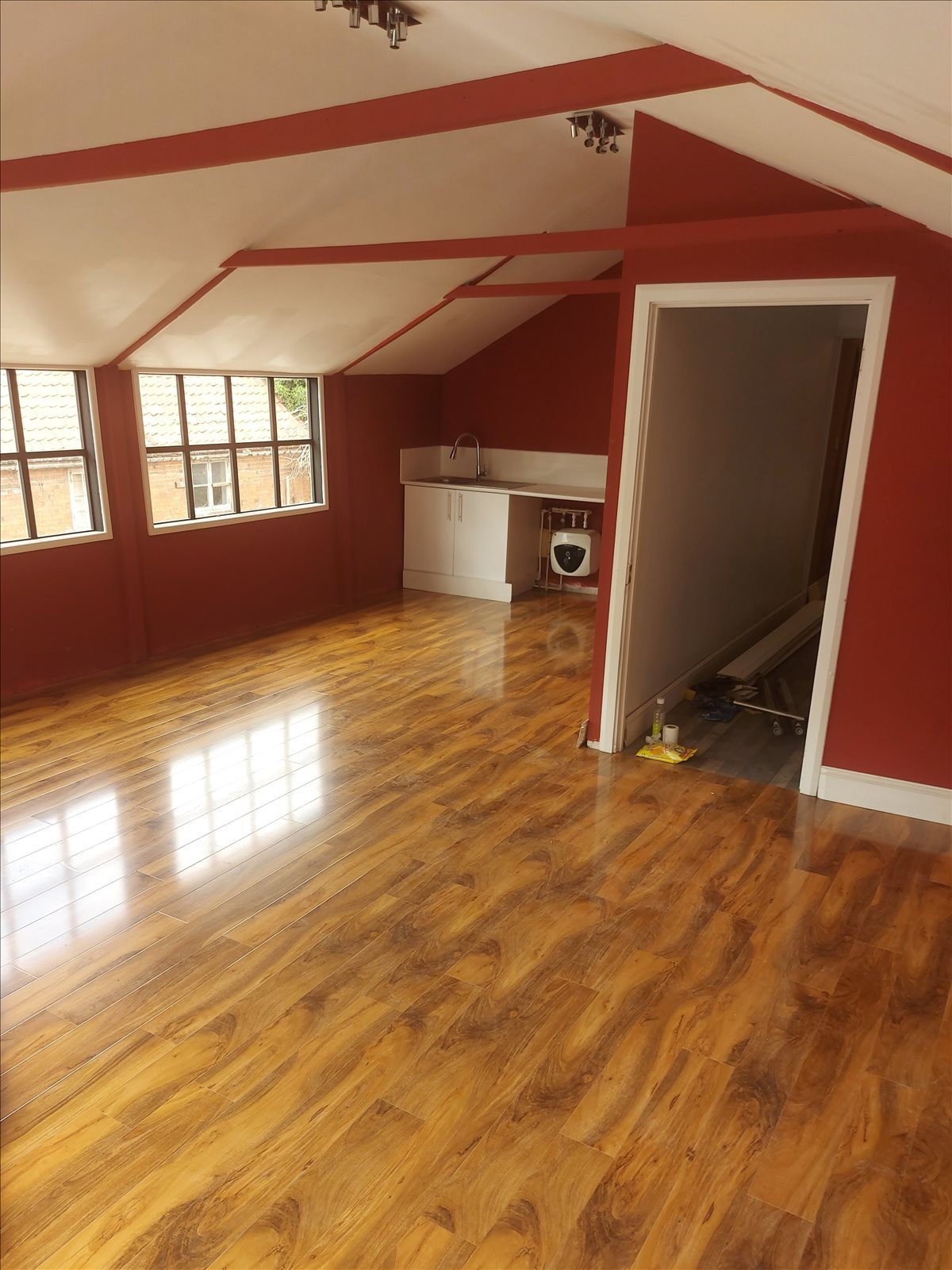 Spacious open-plan room with polished wood floors and red accents.