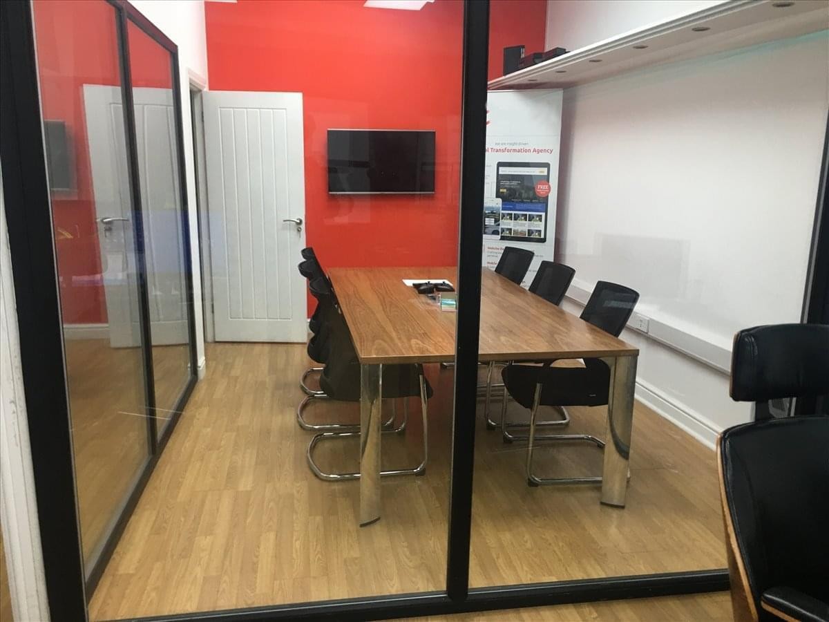 A professional meeting room at 946 Uxbridge Road, Hayes, Uxbridge, Hillingdon featuring a wood table and red accent wall.