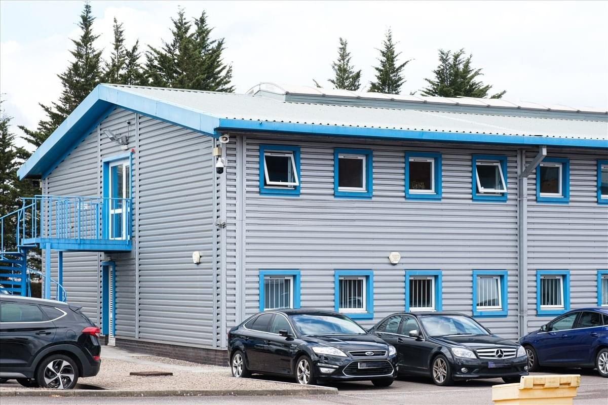 The light grey industrial exterior of Cardiff Bay Business Centre, Lewis Road with blue trim and parked cars.