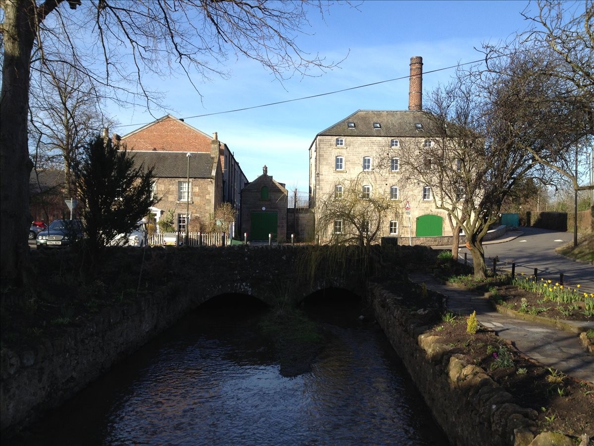 Exterior view of the historic stone and brick facades at Cheviot House, Mill Wynd, with a bridge and stream.