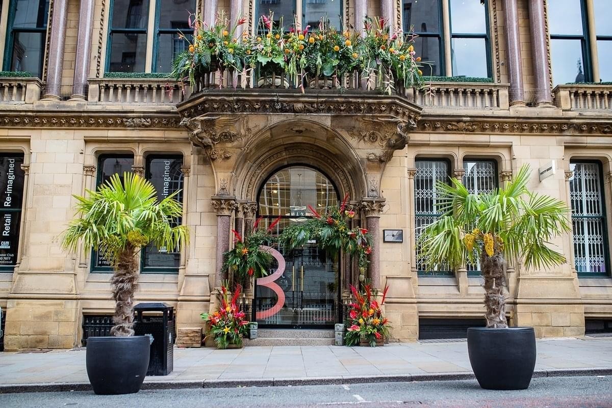 Exterior entrance of Manchester Club, 81 King Street, with stone masonry and potted palm trees.