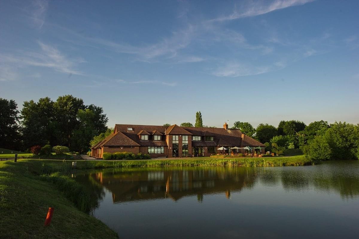 Exterior view of the brick building at Pyrford Golf Club reflecting in the adjacent lake.
