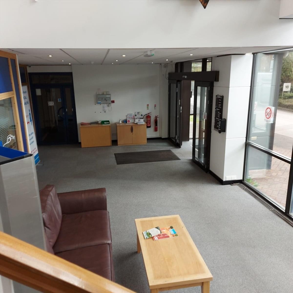 Bright reception lobby with a brown sofa, wooden coffee table, and large windows.