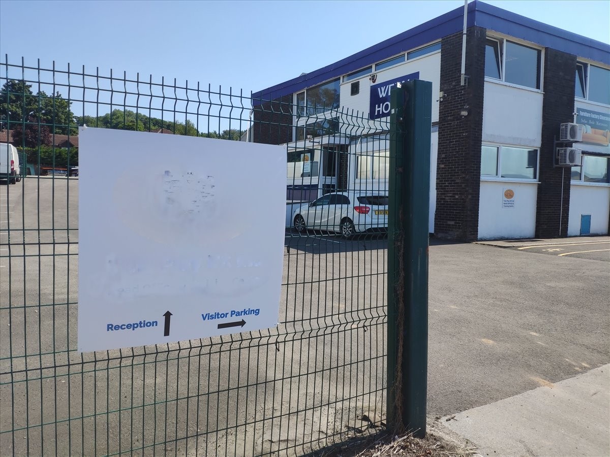 Exterior view of the industrial Wern House building behind a security fence with signage.