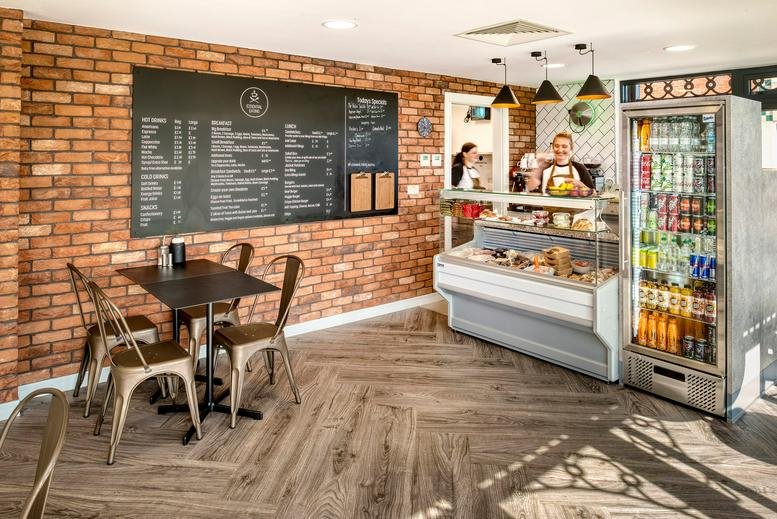 Communal cafe area at Westminster Place with brick walls, chalkboard menus, and a refreshments fridge.