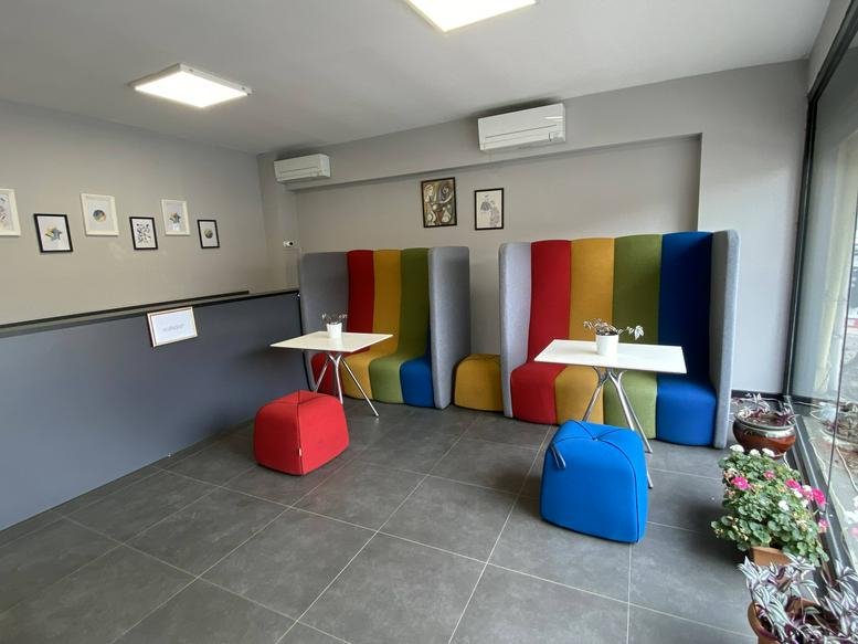 Colorful communal lounge featuring rainbow-striped booths, red and blue ottomans, and small white tables.