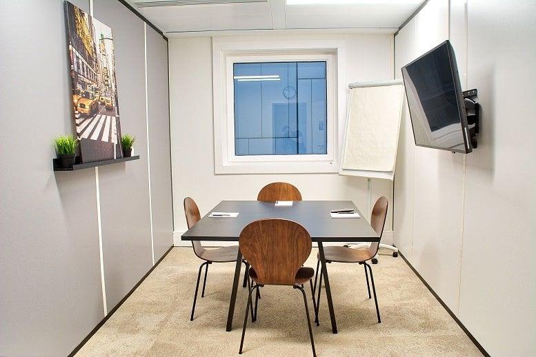 Meeting room with a square table, four wood chairs, and wall-mounted TV.