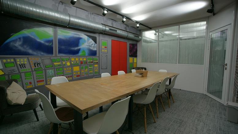 Bright boardroom with a large wooden table, white chairs, and futuristic wall decor.