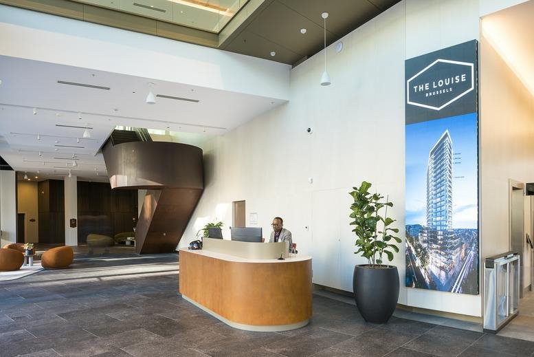 Modern lobby with a wooden curved reception desk, indoor plants, and a large building graphic on the wall.