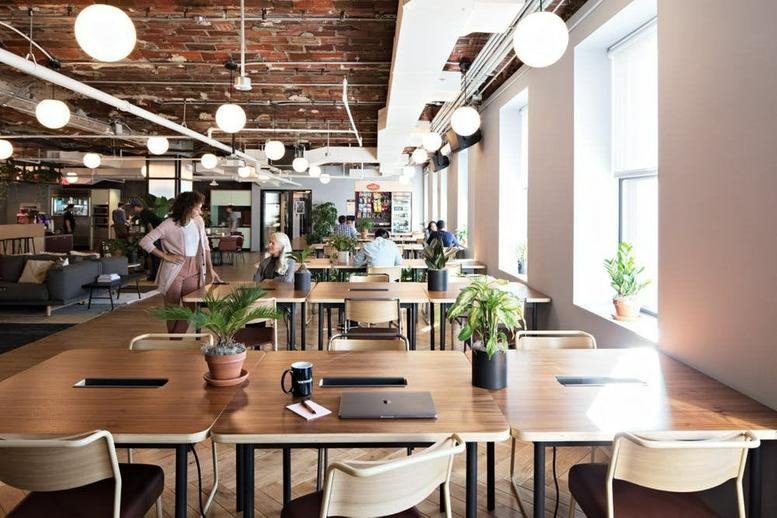 Spacious sunlit coworking area at 18 rue de Navarin, Paris with long wooden tables and exposed brick ceilings.