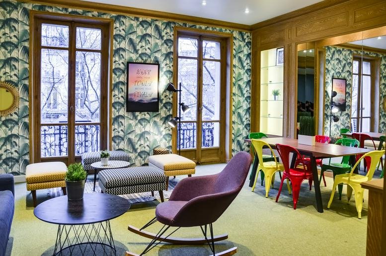 Spacious communal lounge with tropical wallpaper, colorful chairs, and large windows at 18 rue d’Hauteville.
