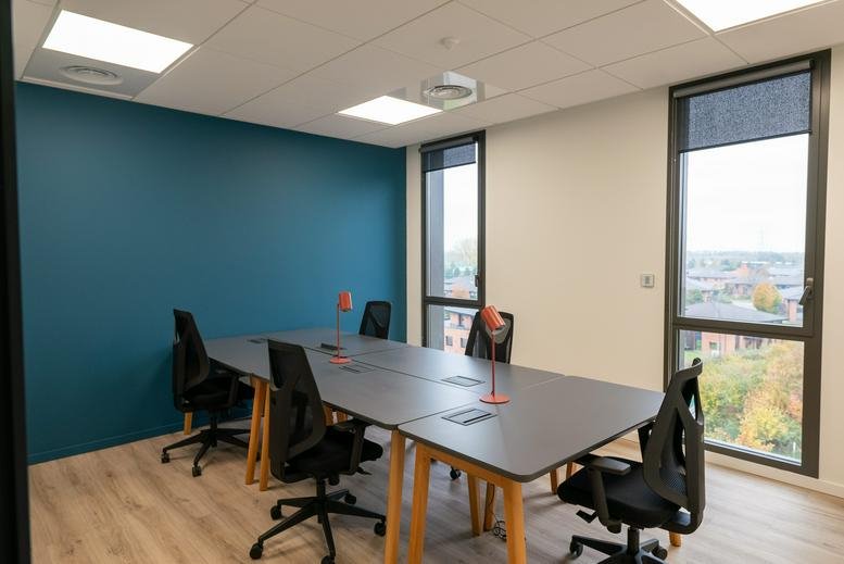 Modern office workspace with dark grey desks and tall windows providing natural light.