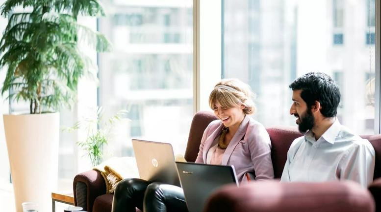 Bright communal lounge at 255 Boulevard Pereire, Paris with a large potted plant and people on laptops.