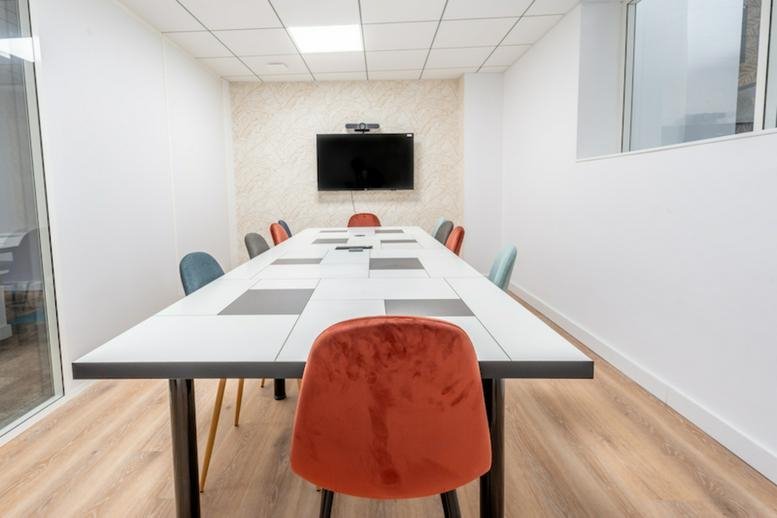 Minimalist conference room with a long white table and coral-colored velvet chairs.