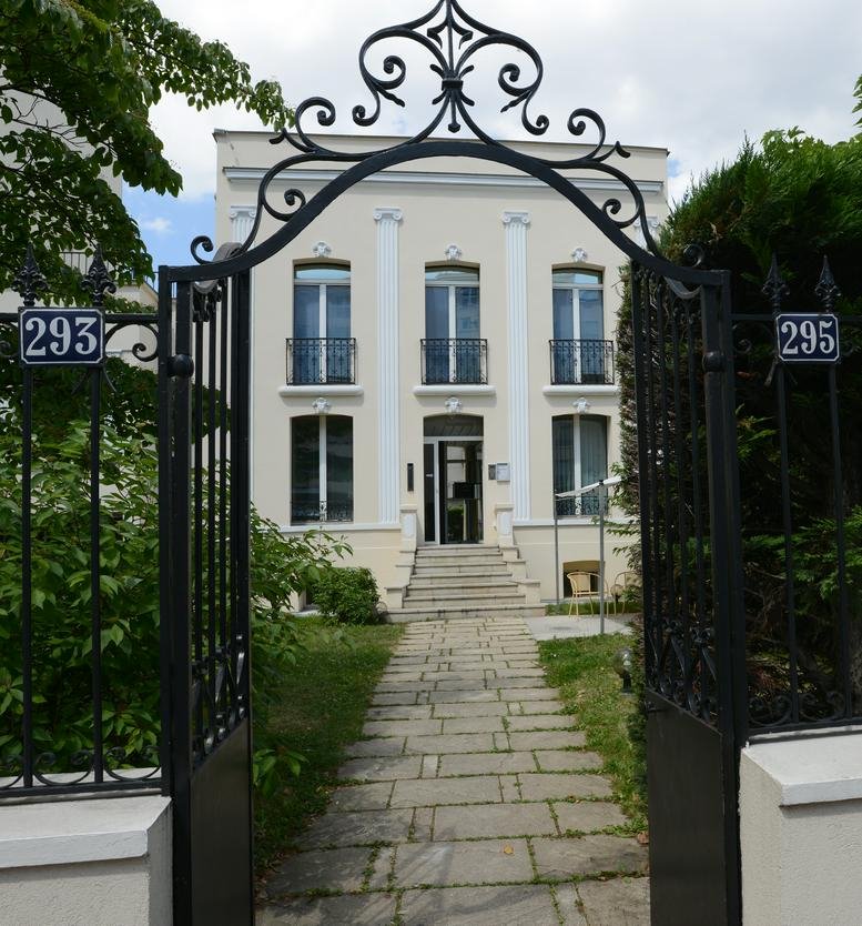 Exterior view of the classic stone facade at 293-295 boulevard Saint Denis, Courbevoie seen through an ornate gate.