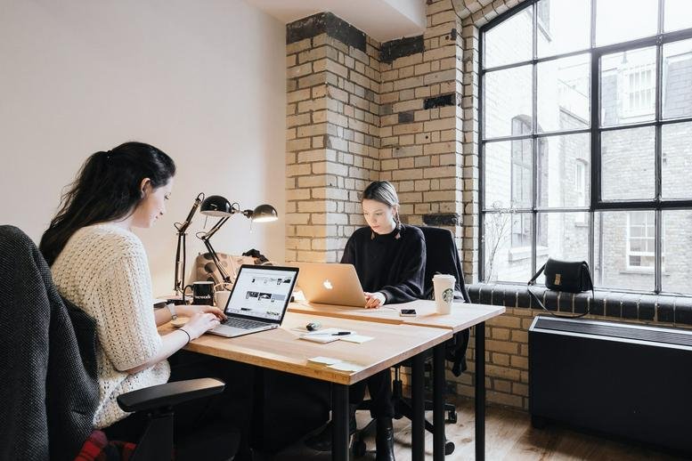 Workspace at 30 Terrasse Bellini with two people working at desks against an exposed brick wall.