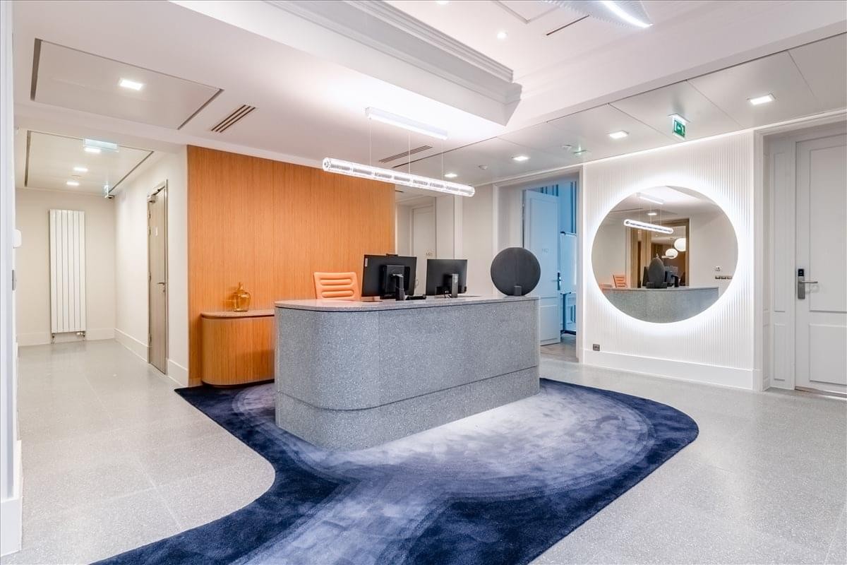 Modern reception area at 32-34 Avenue Kleber, Paris with a grey desk and blue rug.