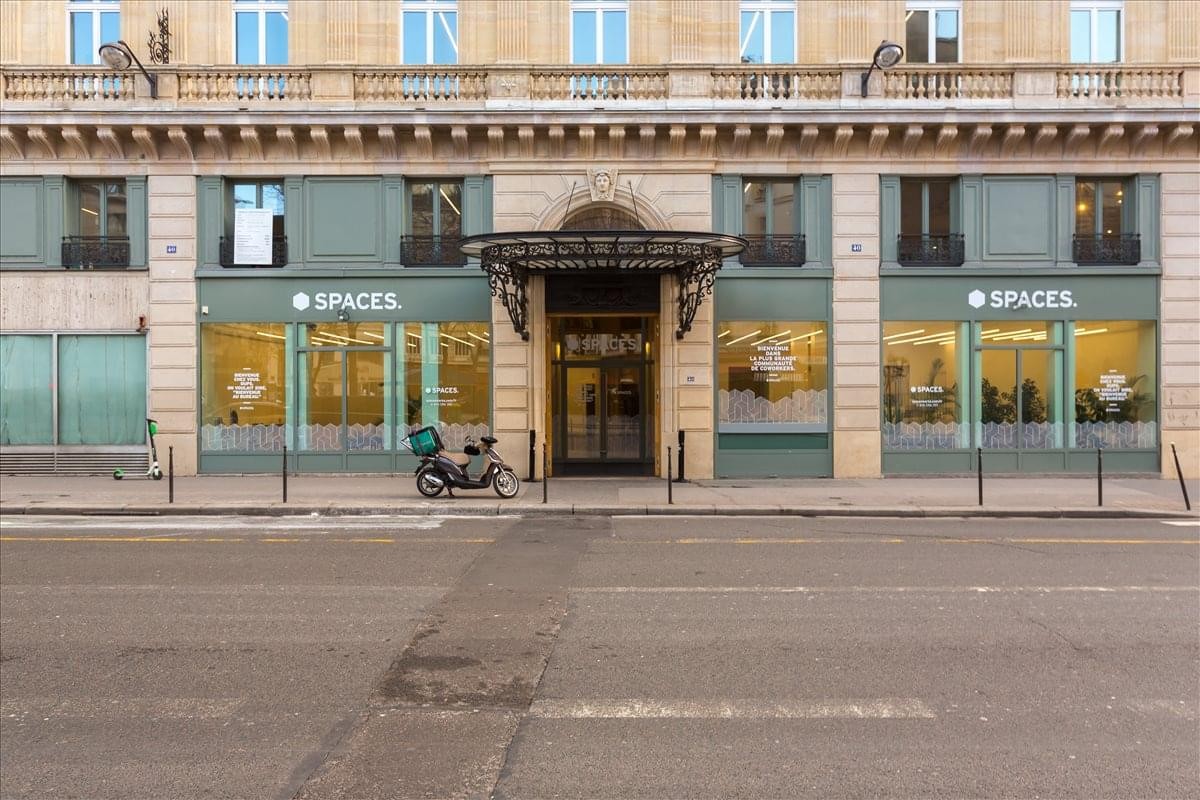 Ground floor exterior of 40 Rue du Louvre, Paris with large glass windows and ornate metal entrance canopy.