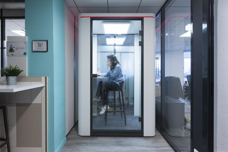 Single-person soundproof phone booth in a modern office with blue accent walls.