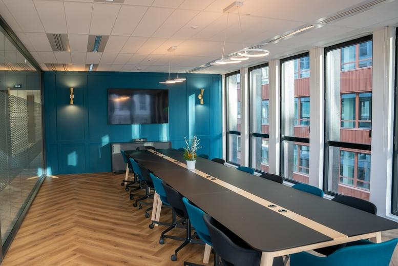 Professional boardroom with a long black conference table, blue chairs, and a large display screen.