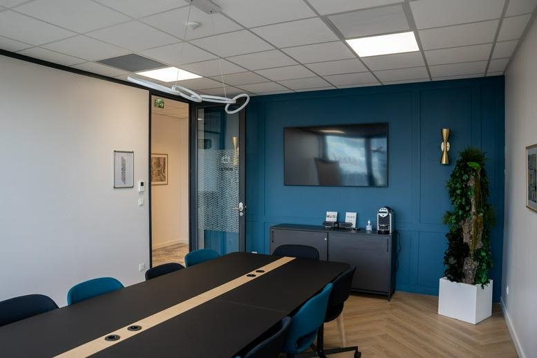 Modern meeting room at 470 Promenade des Anglais with a teal feature wall and long black table.