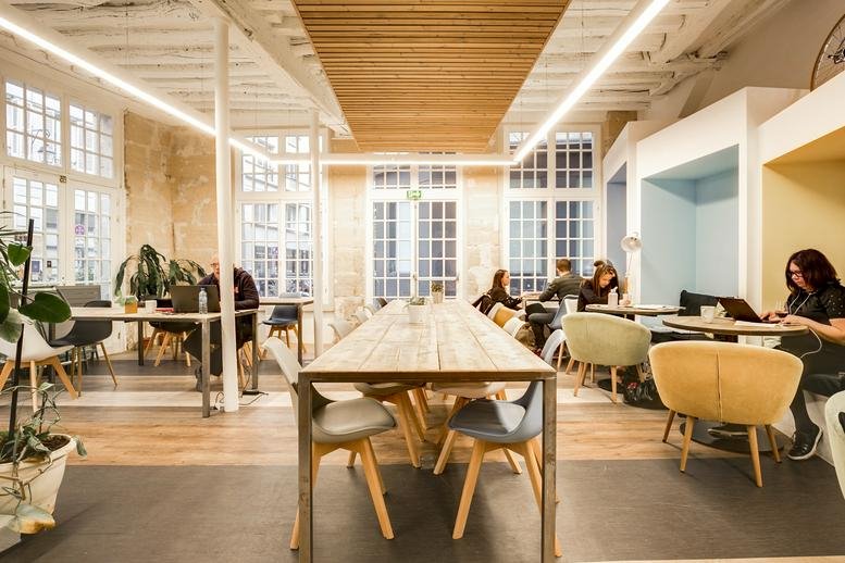 Spacious sun-drenched coworking lounge at 5 Rue du Cloître Saint-Merri with a long wooden table and alcove seating.