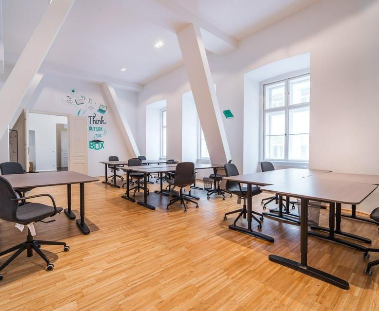 Spacious open-plan office with wooden floors and slanted white support beams.