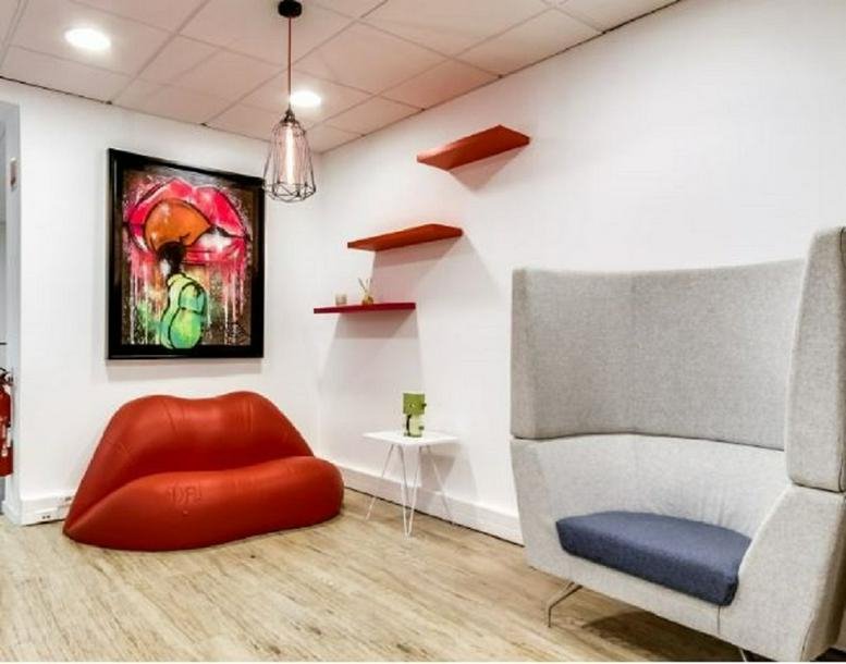 Breakout area at 71 Rue Desnouettes, Paris featuring a red lip-shaped sofa and artistic wall decor.