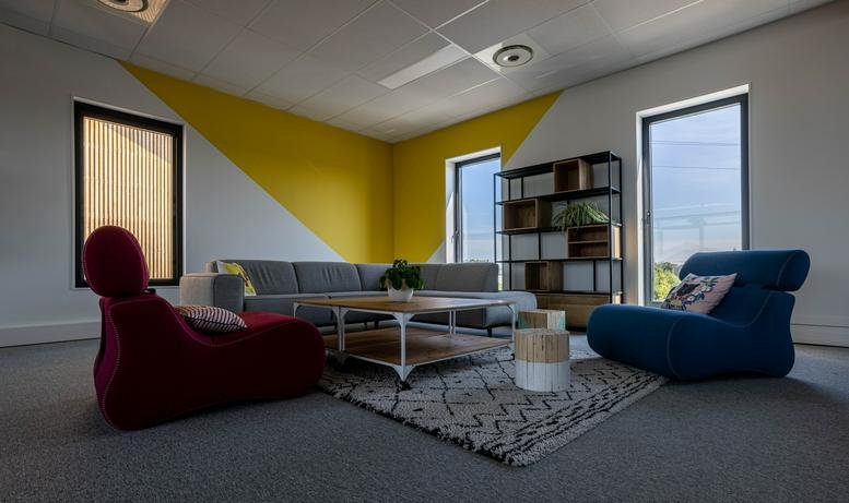 Spacious communal lounge at COLOFT Arteparc Lesquin with colorful seating and a yellow geometric wall mural.